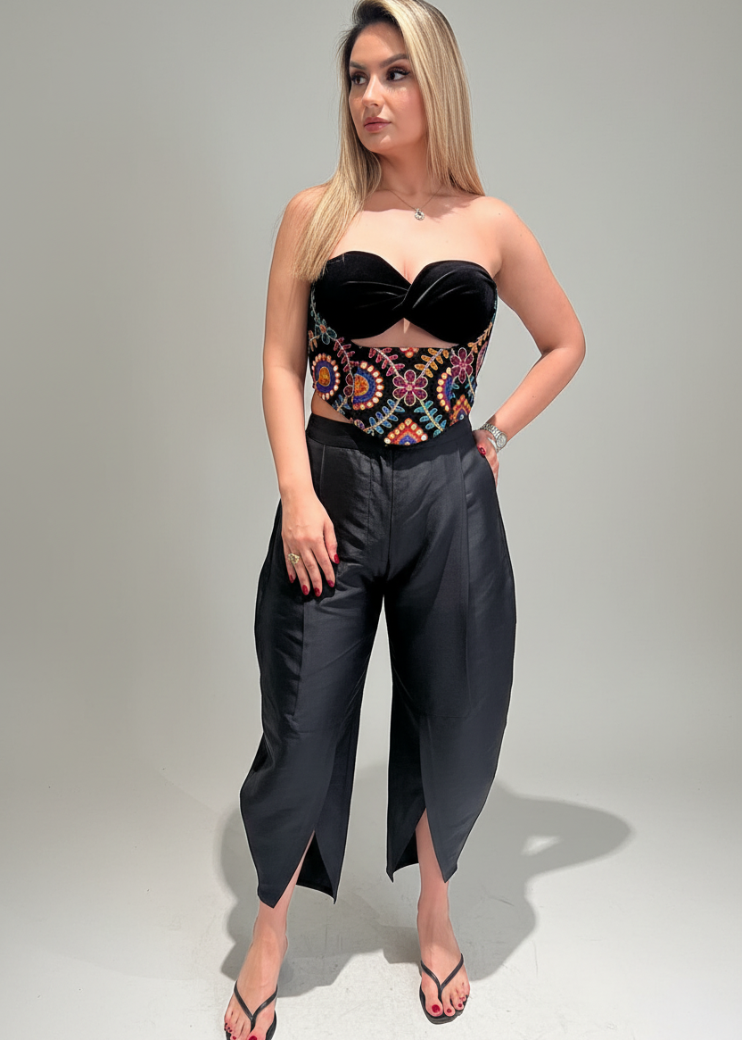Woman wearing a colorful top and dark pants on a plain background