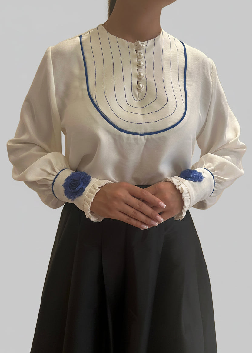 White blouse with blue accents on a plain background