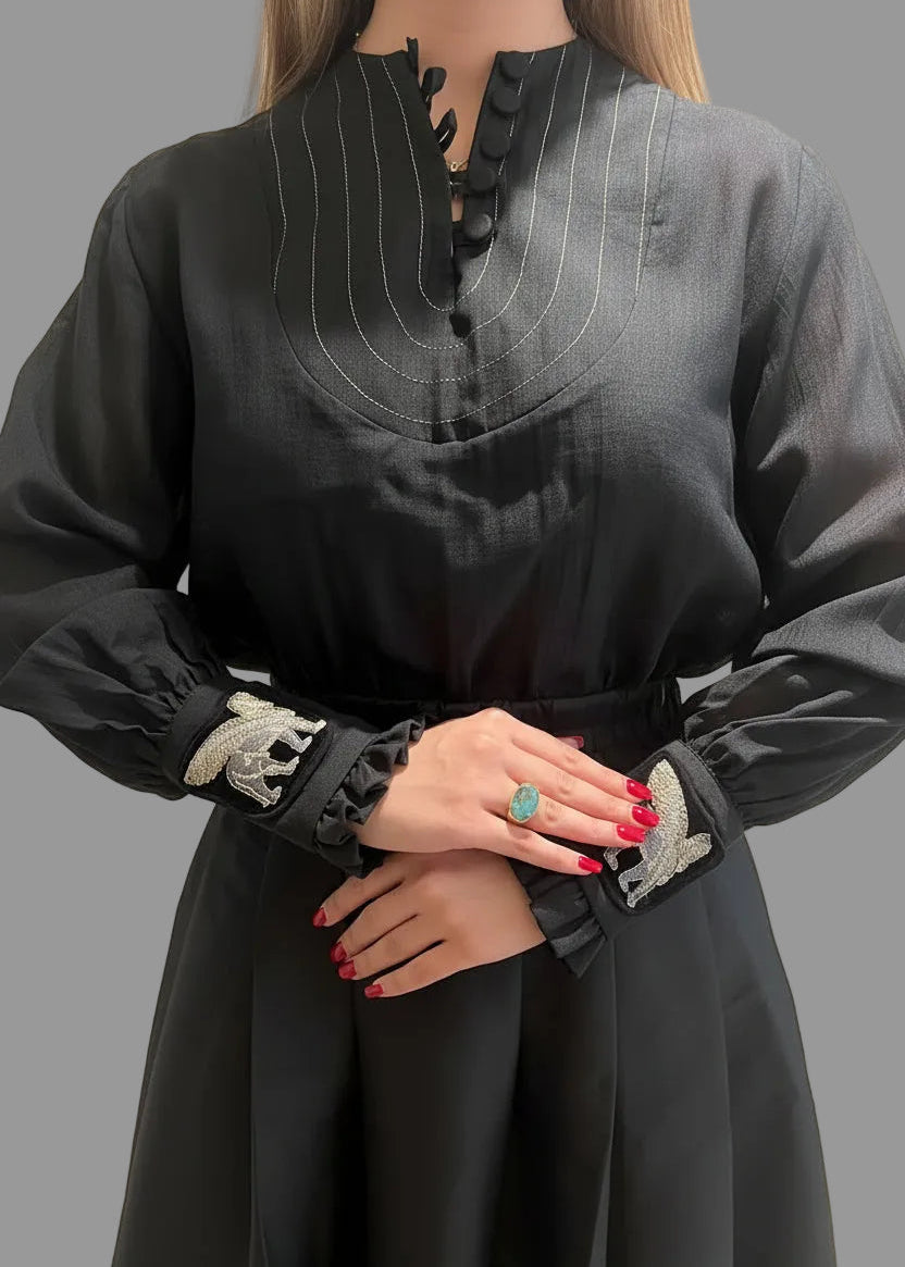 Person wearing a black long-sleeve dress with decorative cuffs on a gray background