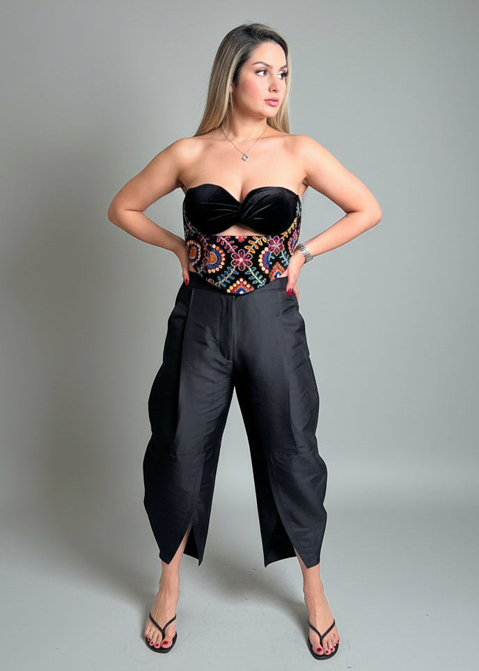 Woman wearing a black strapless top and wide-leg pants with a colorful belt against a gray background