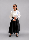 Woman wearing a white blouse with blue trim and a black skirt on a plain background