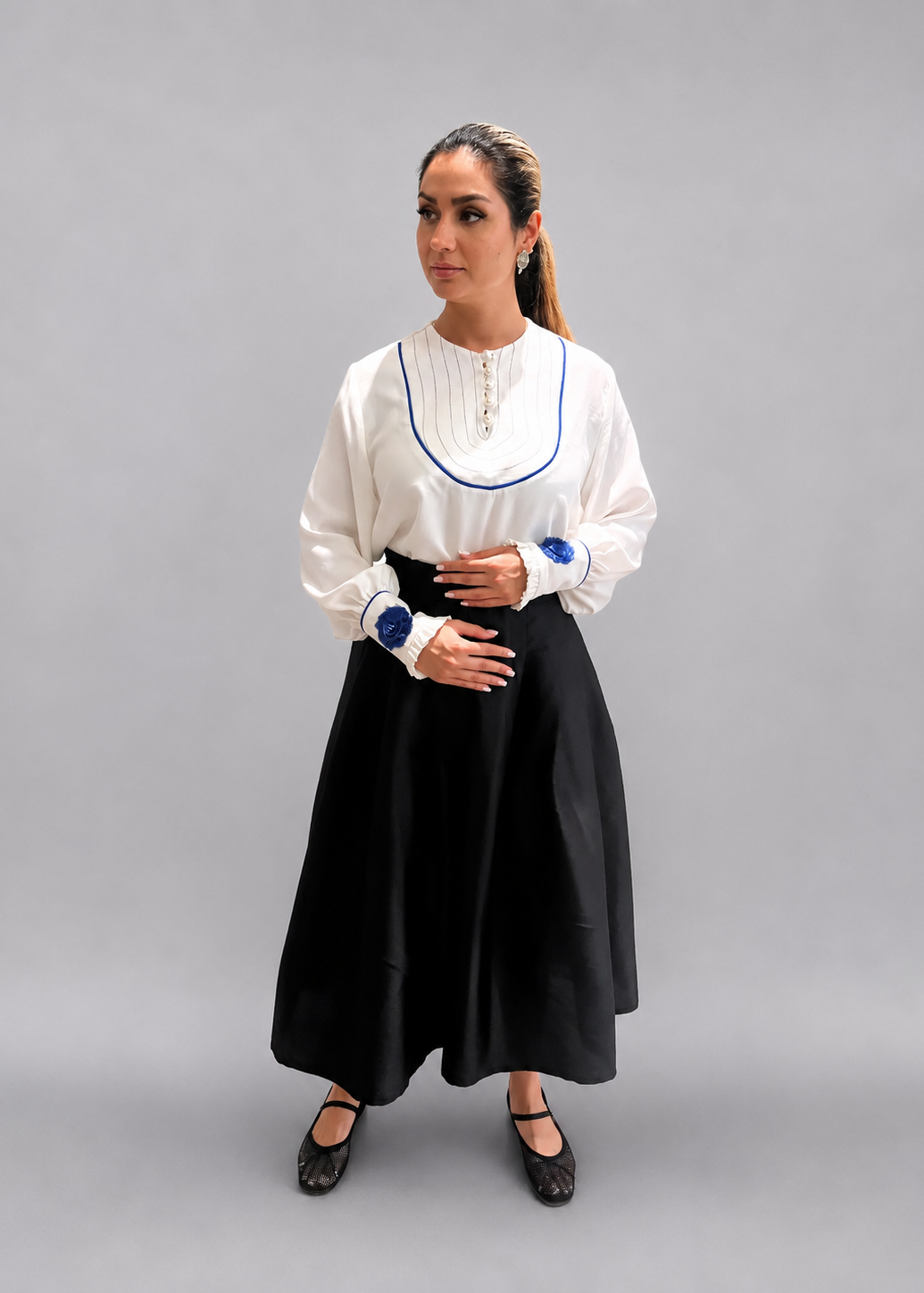 Woman wearing a white blouse with blue trim and a black skirt on a plain background