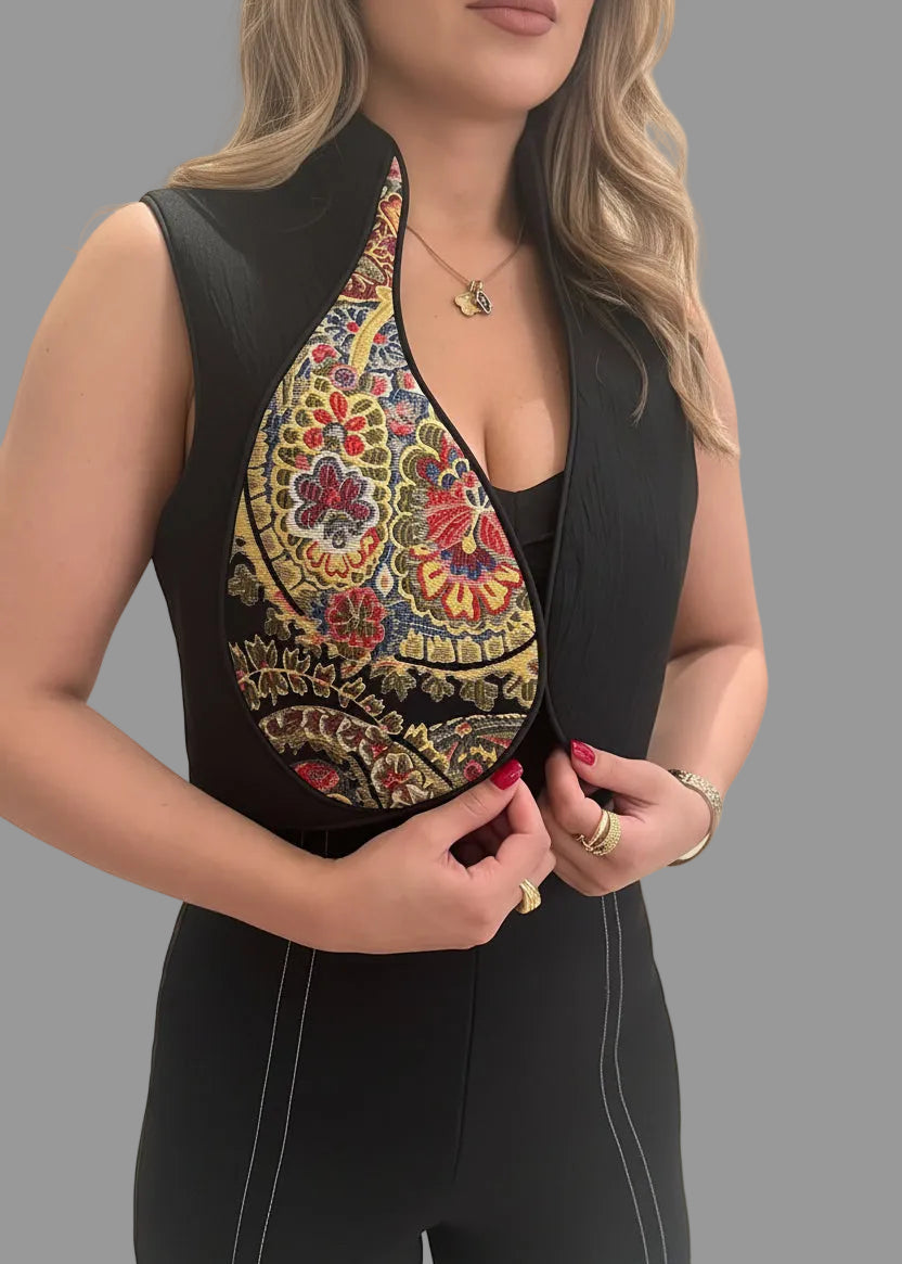Woman wearing a black sleeveless top with colorful embroidered design on a gray background