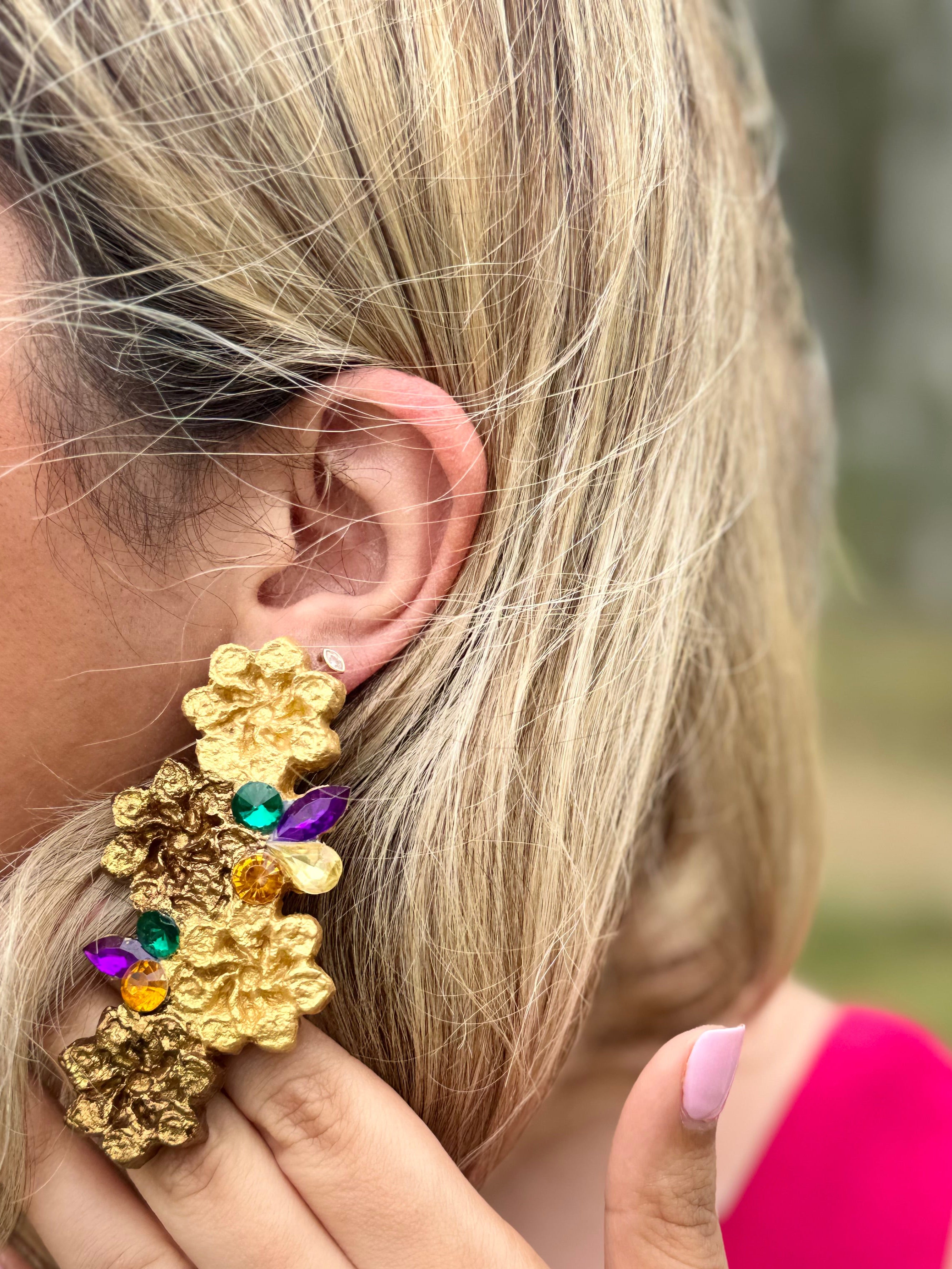 Gold floral earring with colorful stones worn by a person outdoors