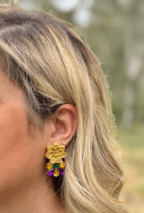 Gold floral earring with colorful stones worn by a person outdoors
