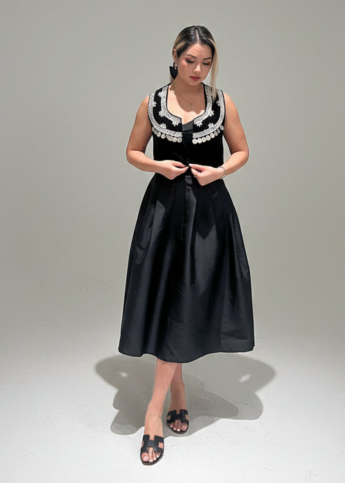 Woman wearing a black dress with white lace details on a gray background