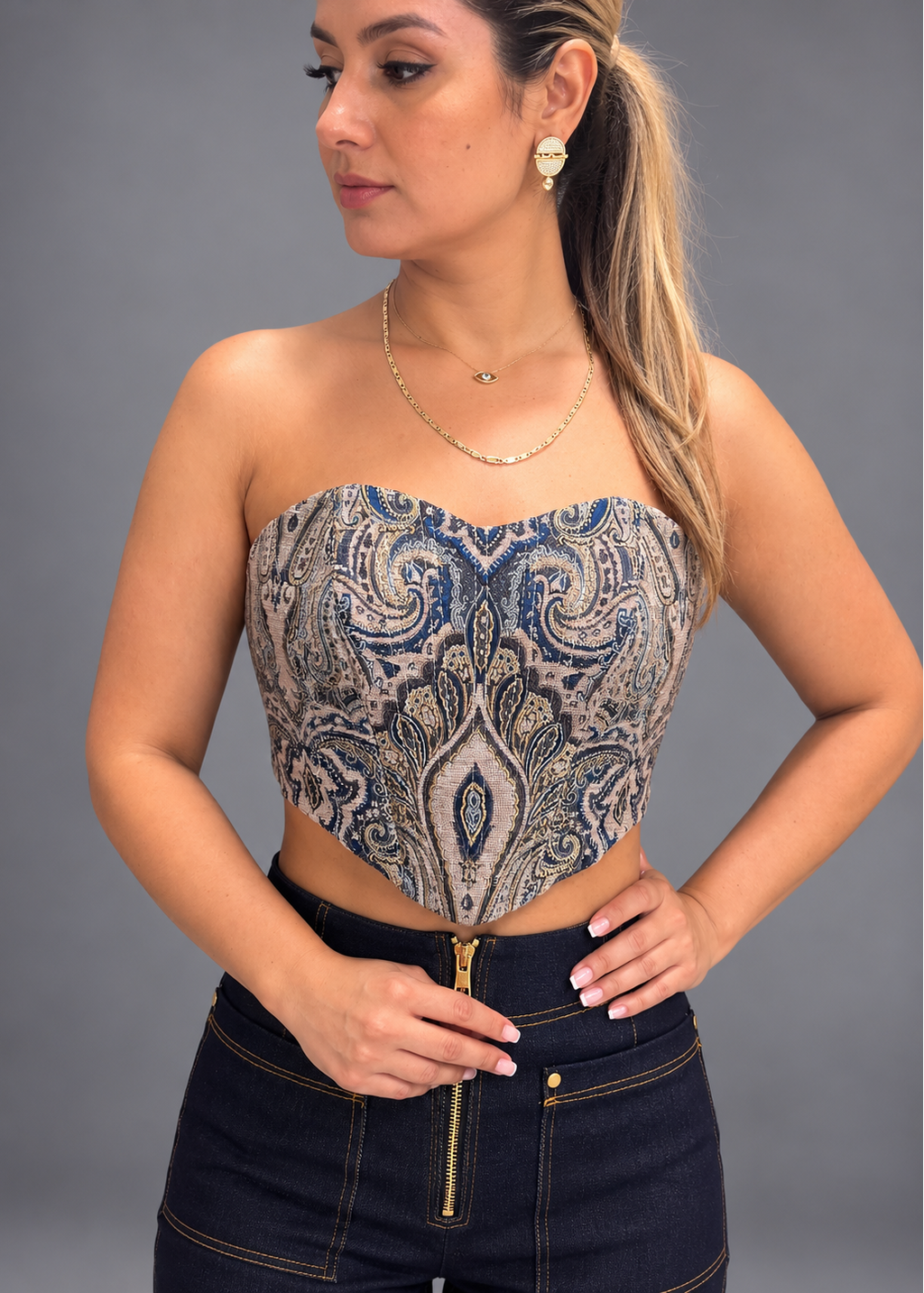 Woman wearing a strapless top with intricate pattern and dark jeans against a gray background
