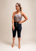Woman wearing a patterned top and dark jeans against a plain 