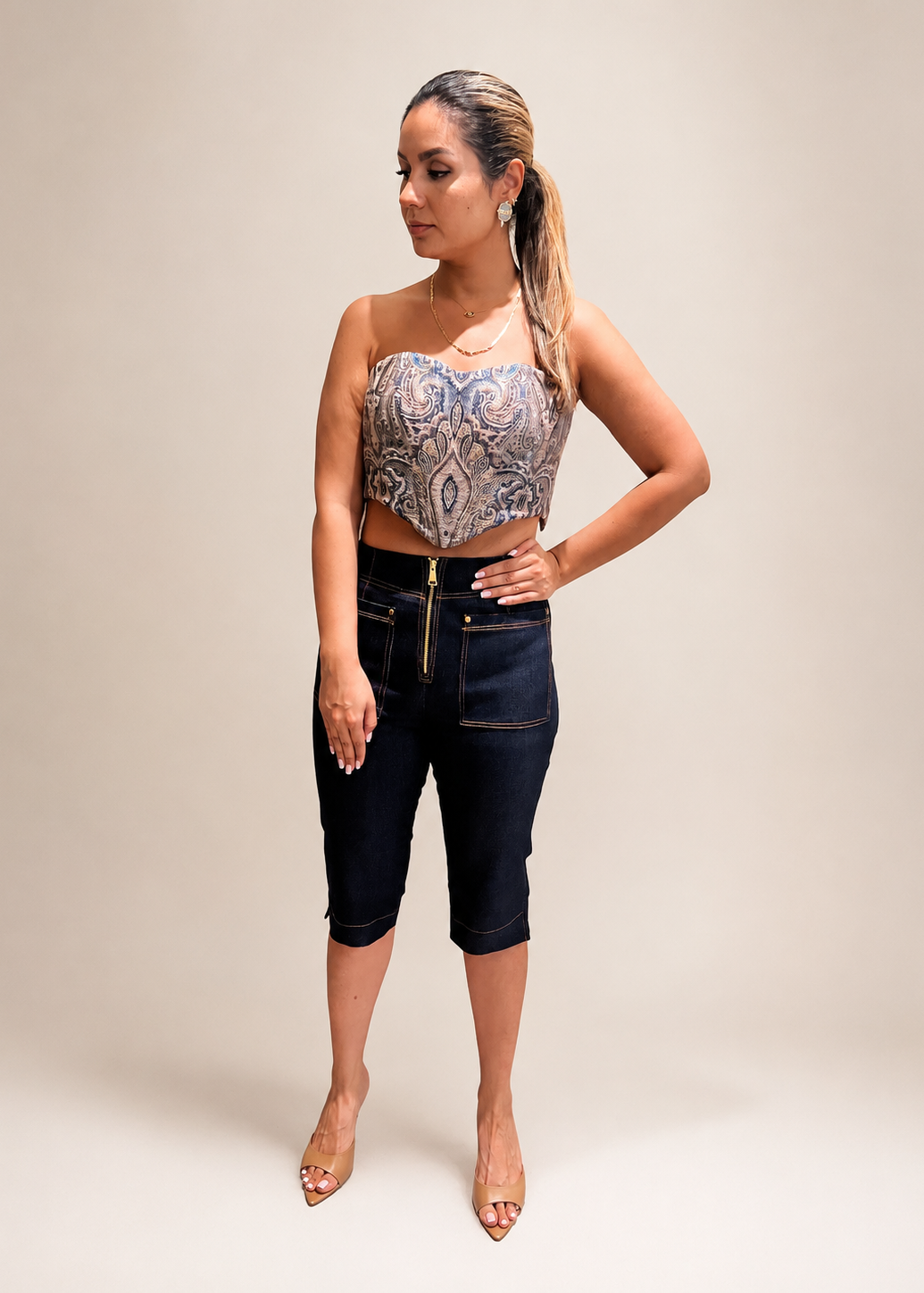 Woman wearing a patterned top and dark jeans against a plain 