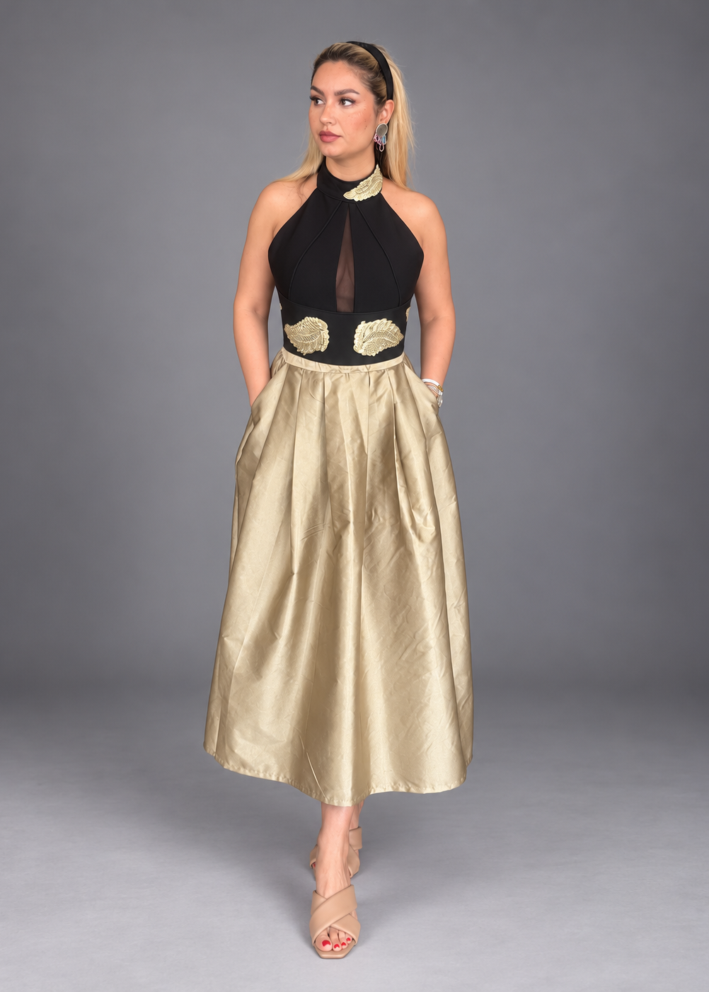 A woman modeling a sleeveless black halter-style bodice, sheer mesh panel, gold applique details, and a voluminous champagne-gold satin skirt