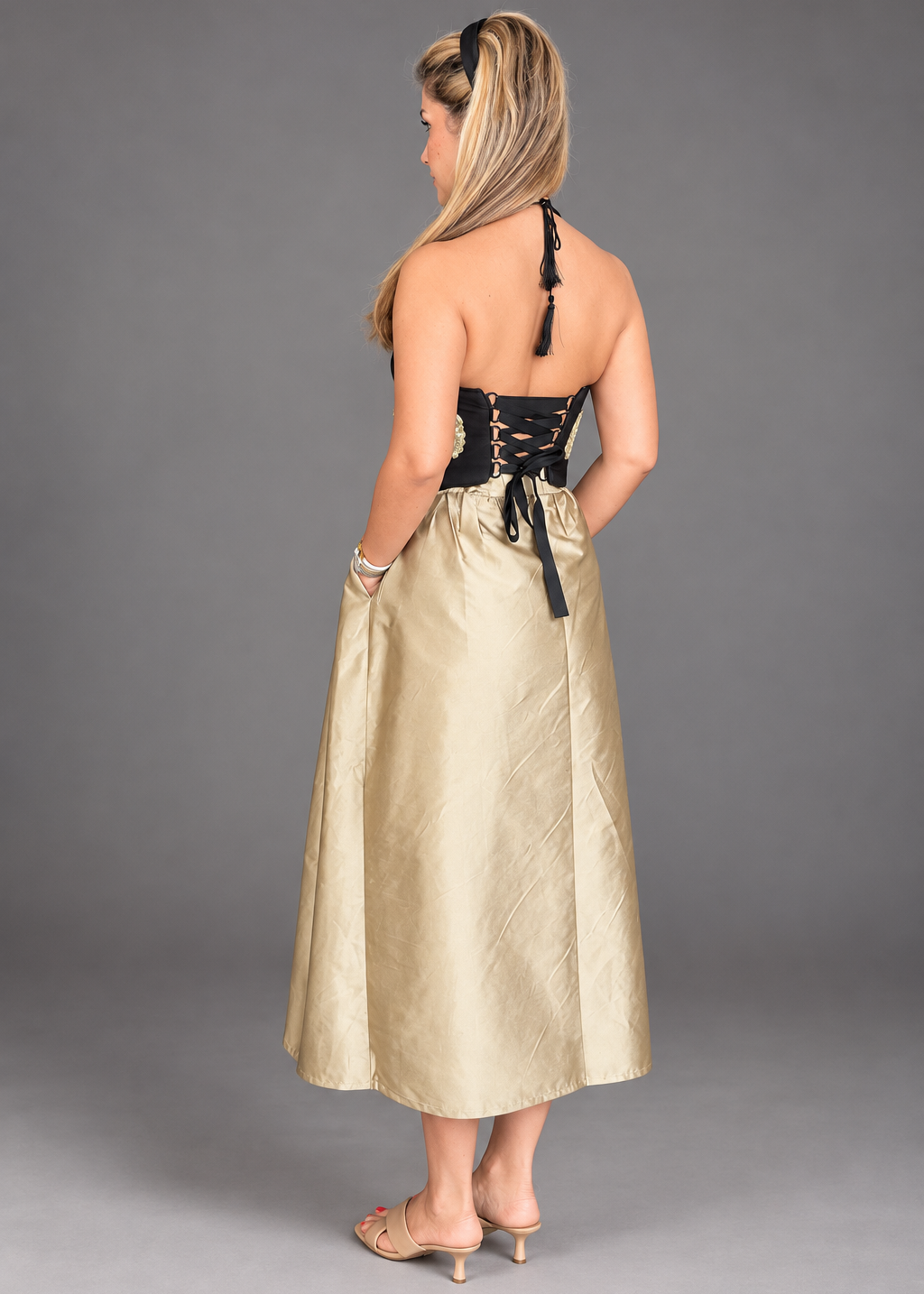 A woman modeling a sleeveless black halter-style bodice, sheer mesh panel, gold applique details, and a voluminous champagne-gold satin skirt