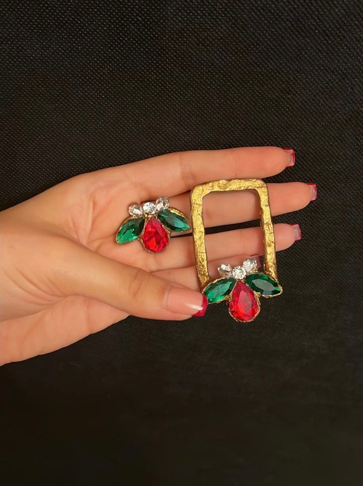 Gold brooch with red and green gemstones held in a hand against a black background
