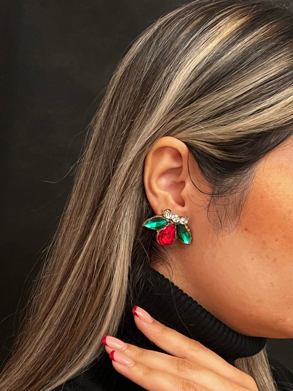 Close-up of a person wearing colorful gemstone earrings against a black background