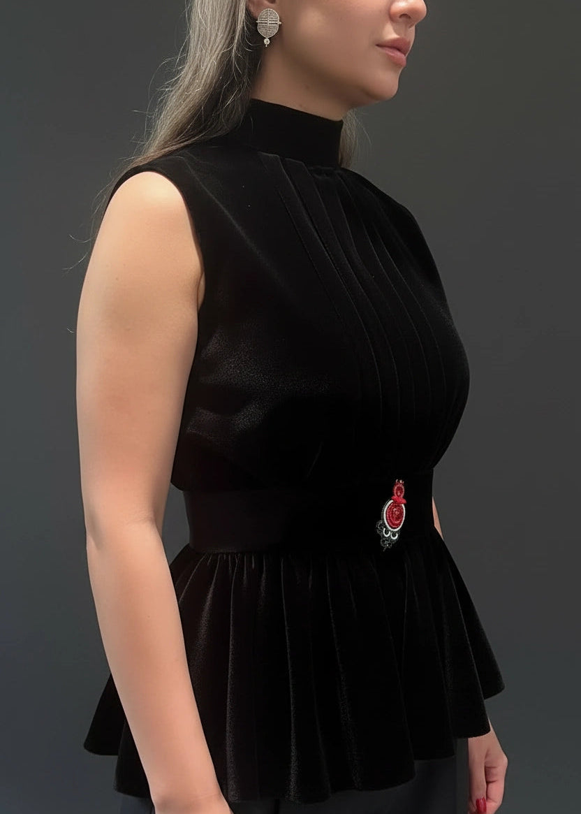 Woman wearing a black sleeveless top with a decorative brooch on a dark background