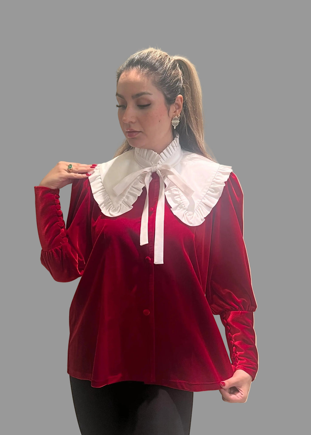 Woman wearing a red velvet blouse with a white collar against a gray background
