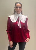 Woman wearing a red blouse with a white ruffled collar against a plain background