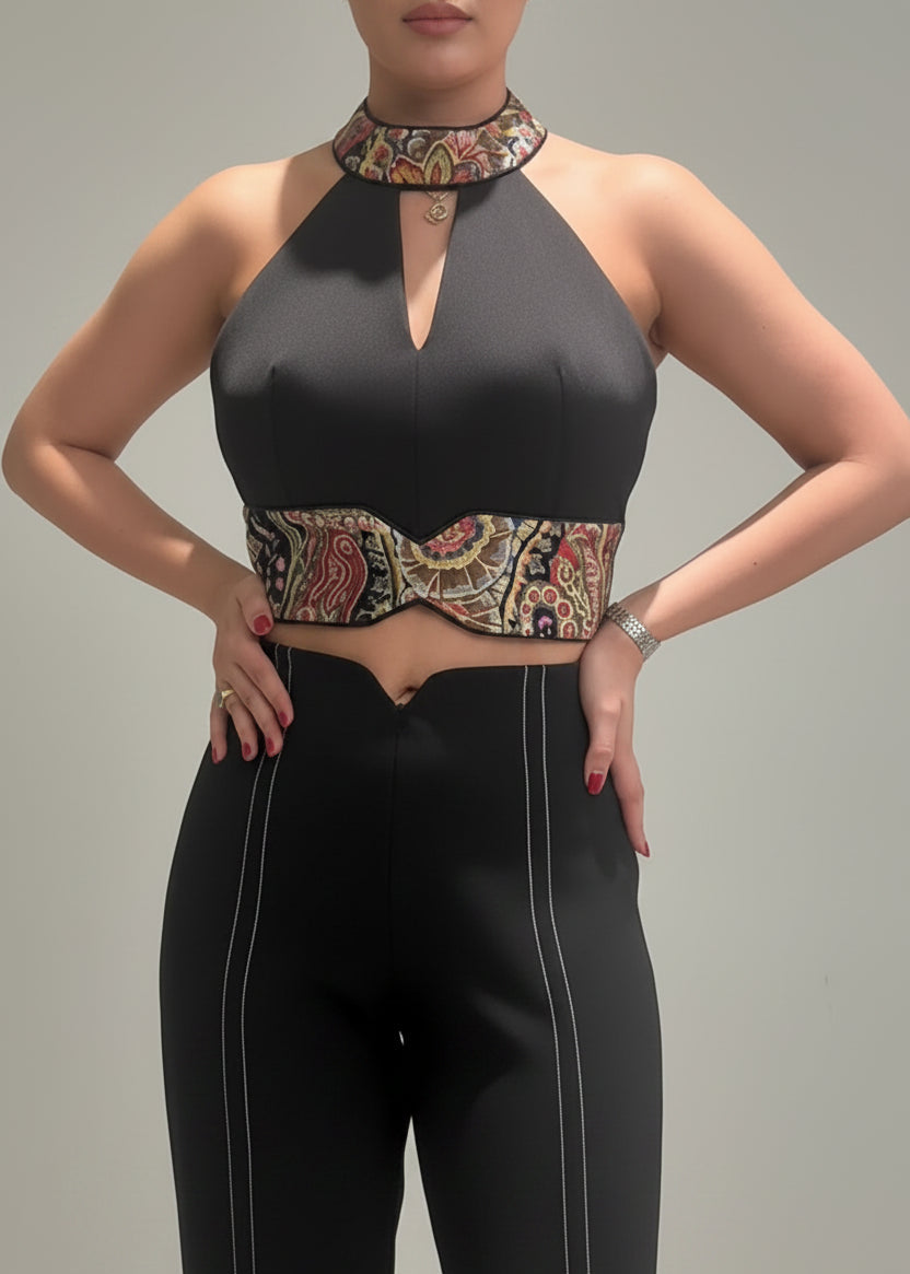 Person wearing a black halter top with patterned accents and black pants on a plain background