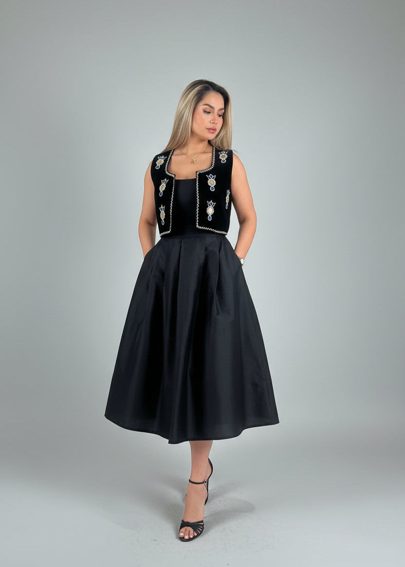 Woman wearing a black dress with floral embroidery on a gray background