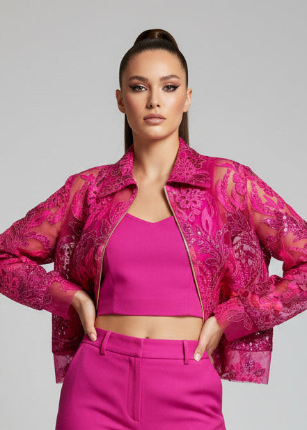 Woman wearing a bright pink outfit with a sheer jacket on a gray background