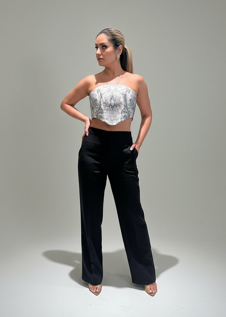 Woman wearing a patterned top and black pants standing in a room with a neutral wall.