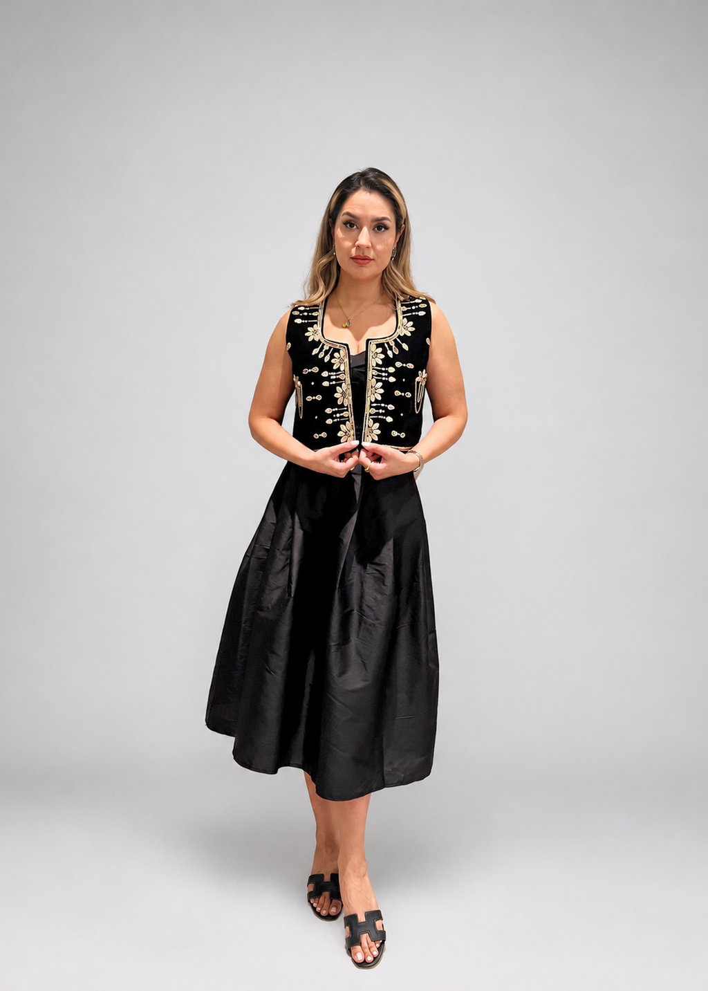 Woman wearing a black dress with gold detailing against a gray background