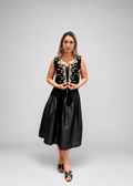 Woman wearing a black dress with gold detailing against a gray background