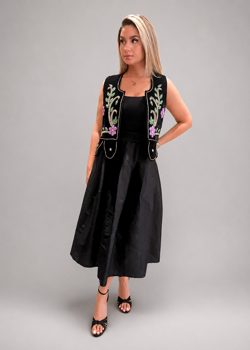 Woman wearing a black dress with an embroidered vest against a gray background