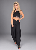 A woman modeling a black two-piece outfit consisting of a halter crop top with lace cutouts and matching wide-leg pants, photographed against a solid gray studio background.