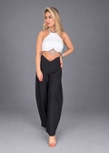 A woman modeling a white halter crop top with a lace waist detail and black wide-leg pants against a solid gray studio background.