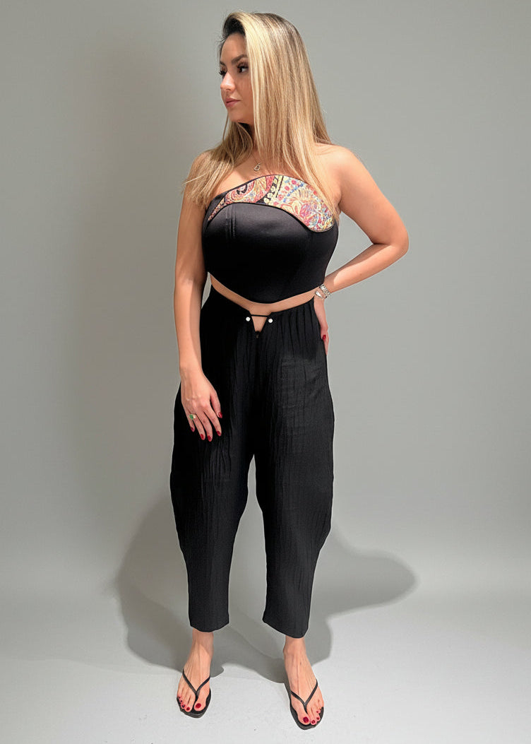 Woman wearing a black strapless top with colorful pattern and high-waisted black pants on a gray background
