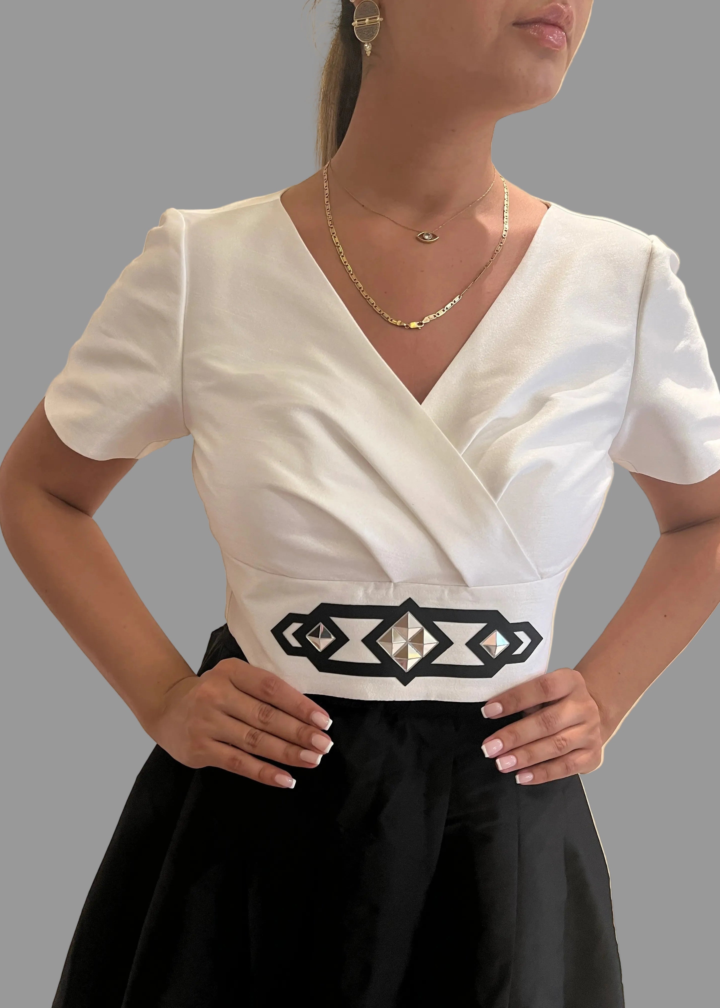 Woman wearing a white top with a black belt and black skirt on a gray background