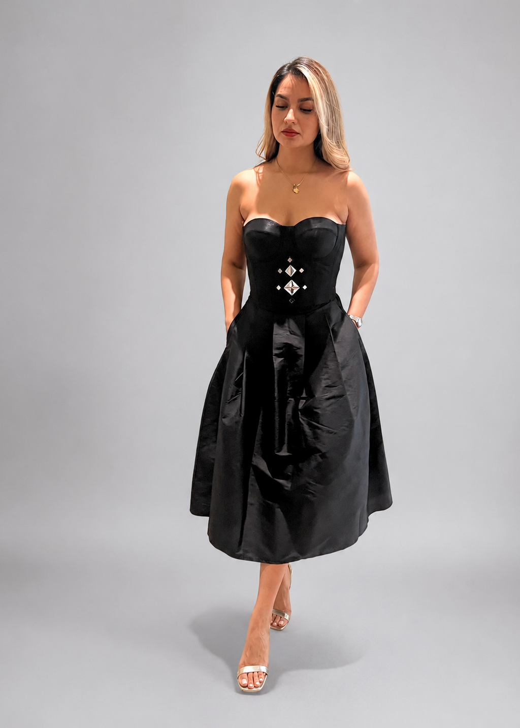 Woman wearing a black strapless dress with a corset-style waist on a gray background