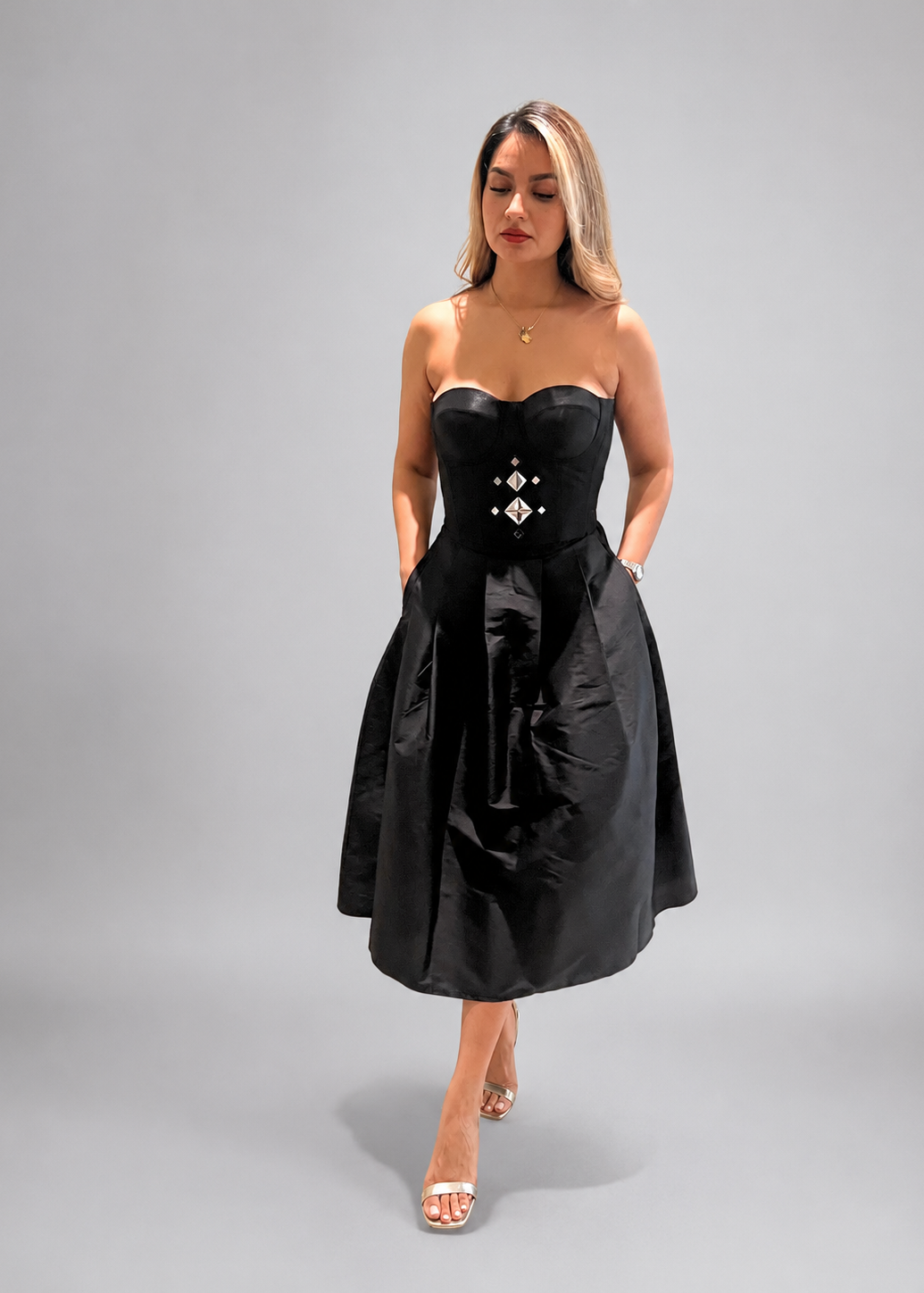 Woman wearing a black strapless dress with a corset-style waist on a gray background