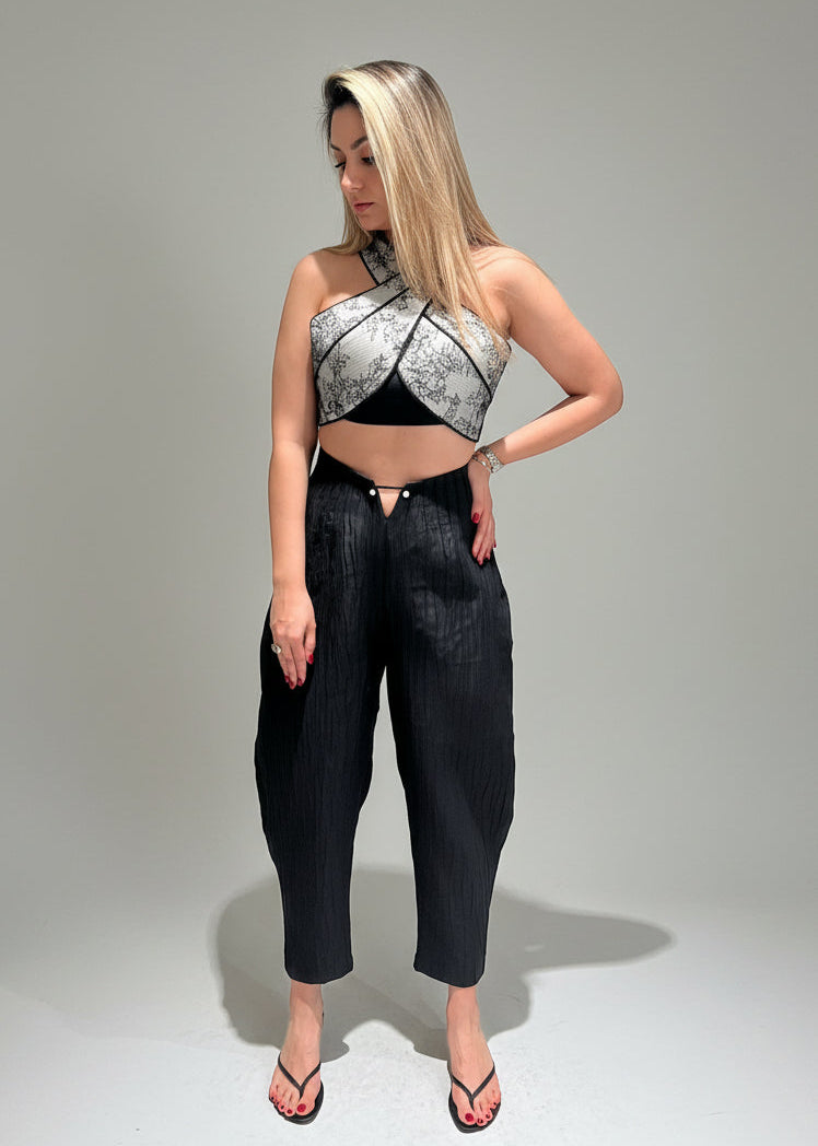 Woman wearing a black and white patterned top and black pants on a gray background