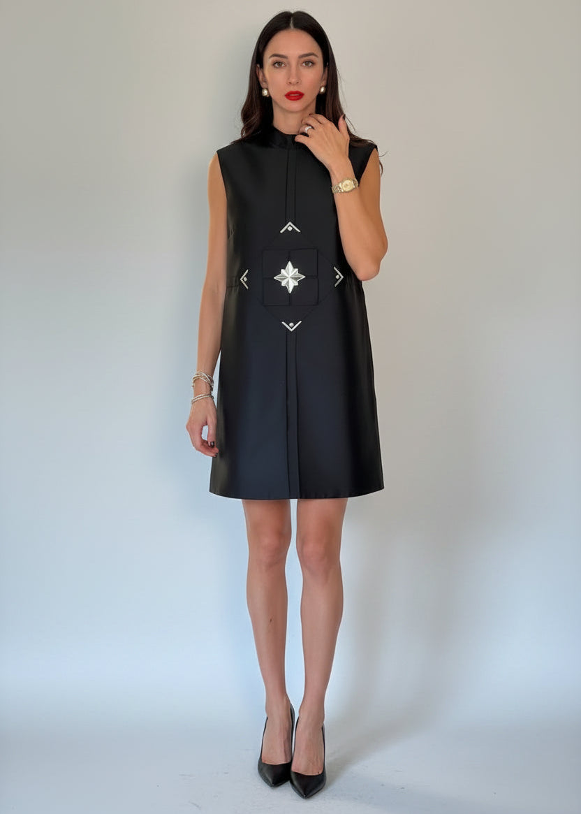 Woman wearing a black sleeveless dress with white patterns on a plain background