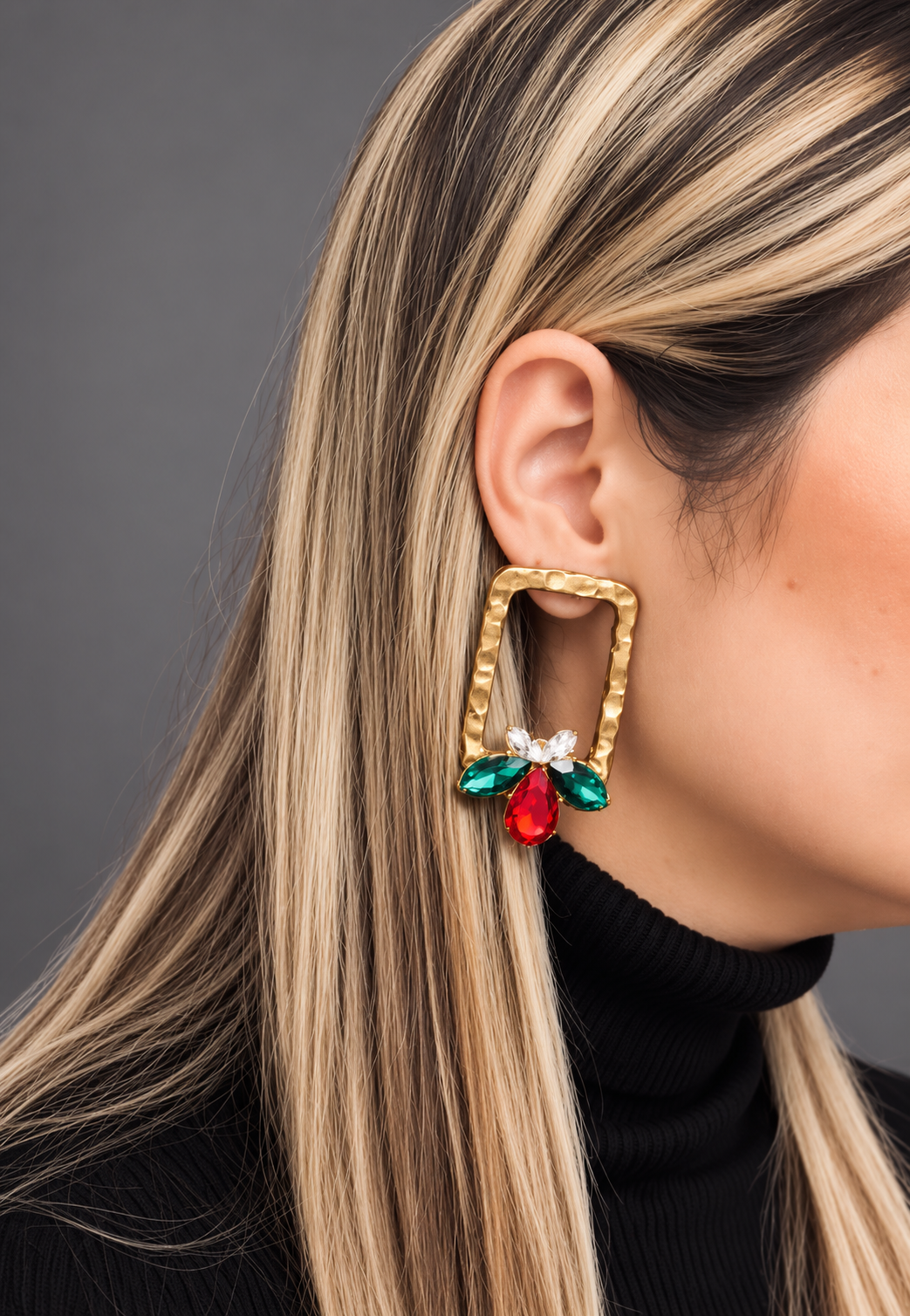 Close-up of a person wearing colorful gemstone earrings against a black background