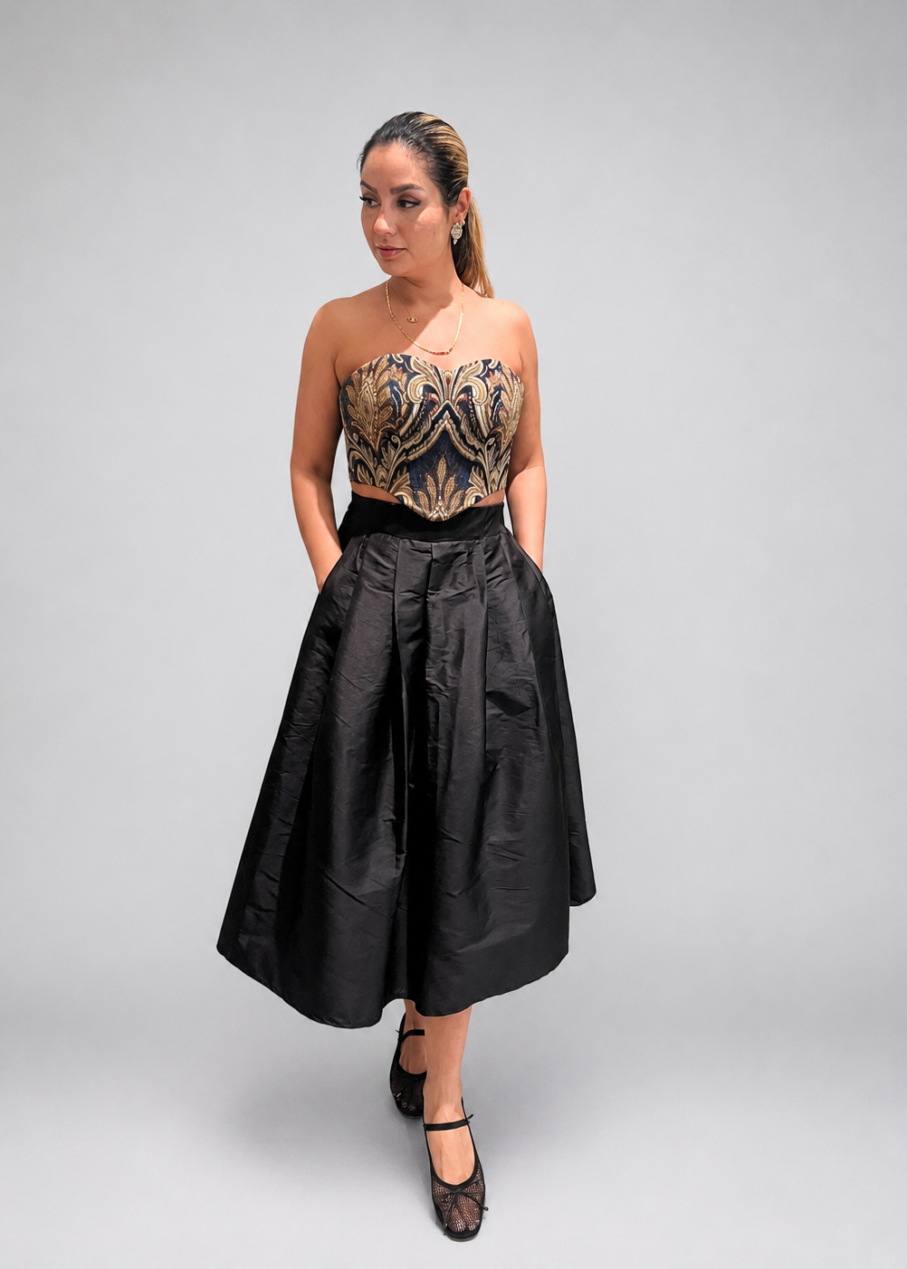 Woman wearing a strapless embroidered top and black skirt against a neutral background