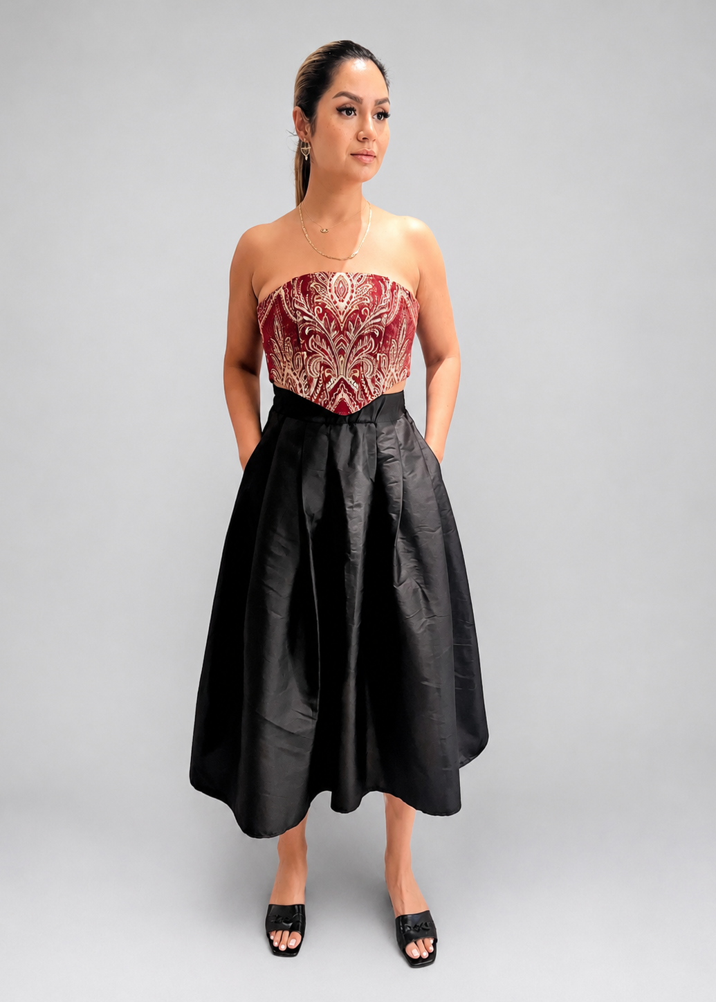 Woman wearing a strapless red and gold top with a black skirt on a plain background
