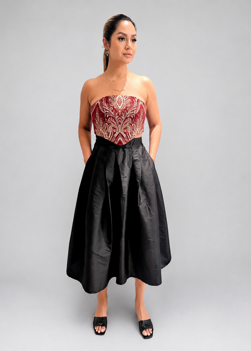 Woman wearing a strapless red and gold top with a black skirt on a plain background