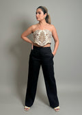 Woman wearing a strapless top with intricate design and black pants against a gray background