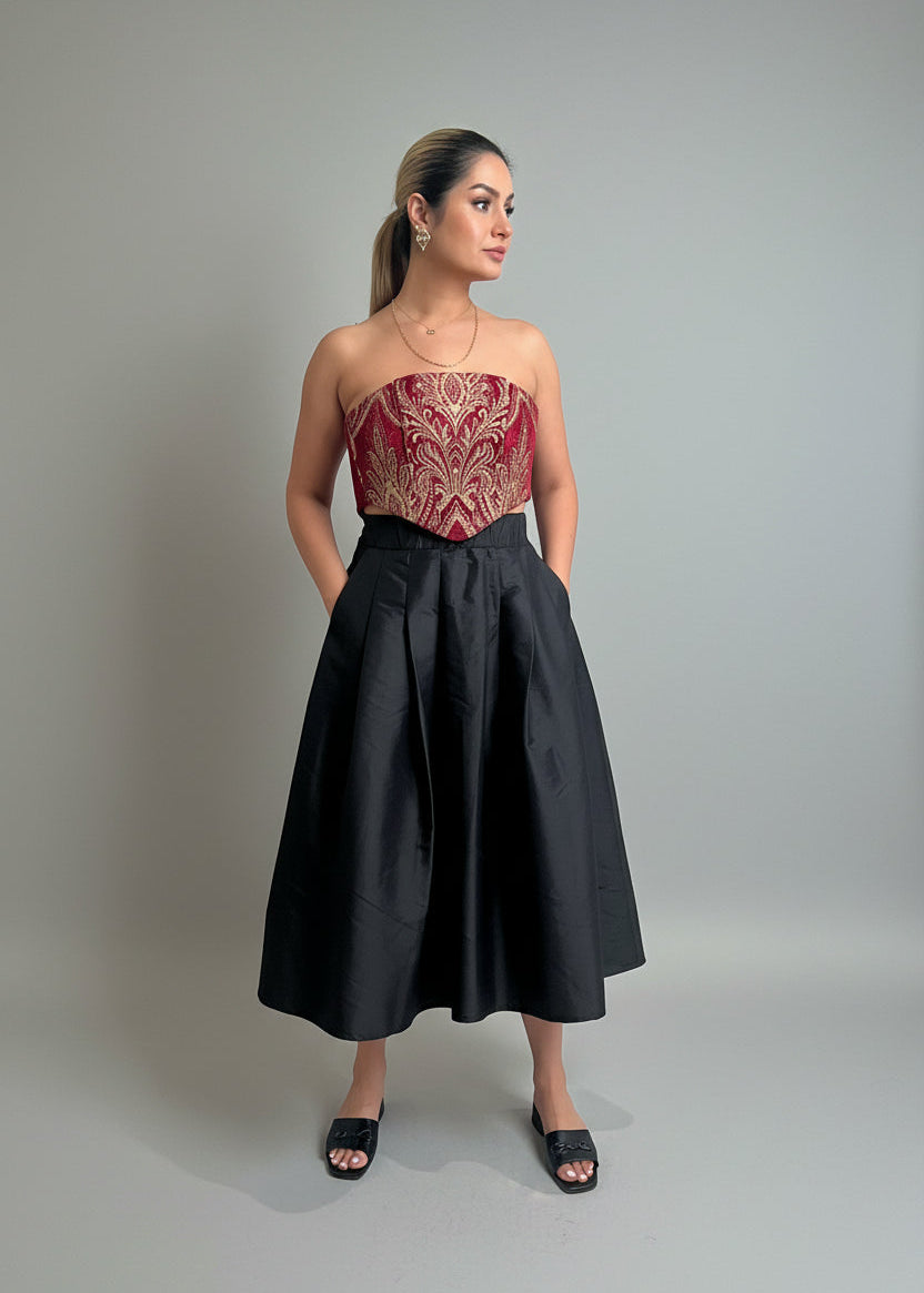 Woman wearing a strapless red and gold top with a black skirt on a plain background