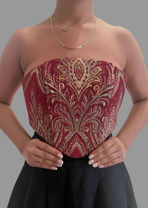 Red strapless top with gold embroidery worn by a person on a gray background