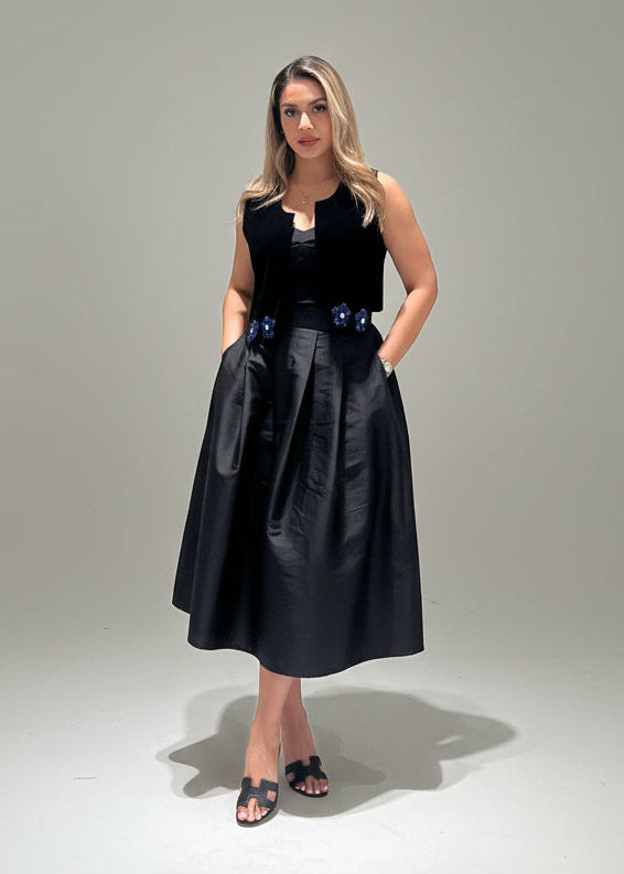 Woman wearing a black sleeveless top and black skirt with floral details on a gray background