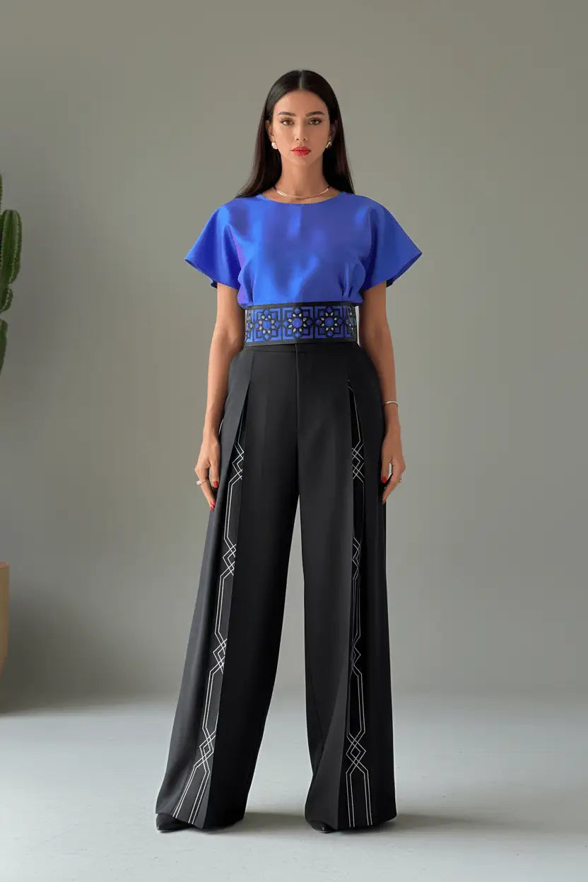 Woman wearing a blue top and black pants with geometric patterns on a neutral background