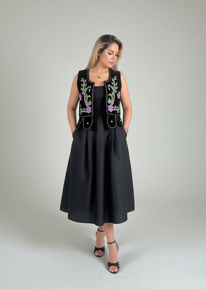 Woman wearing a black dress with embroidered vest on a gray background