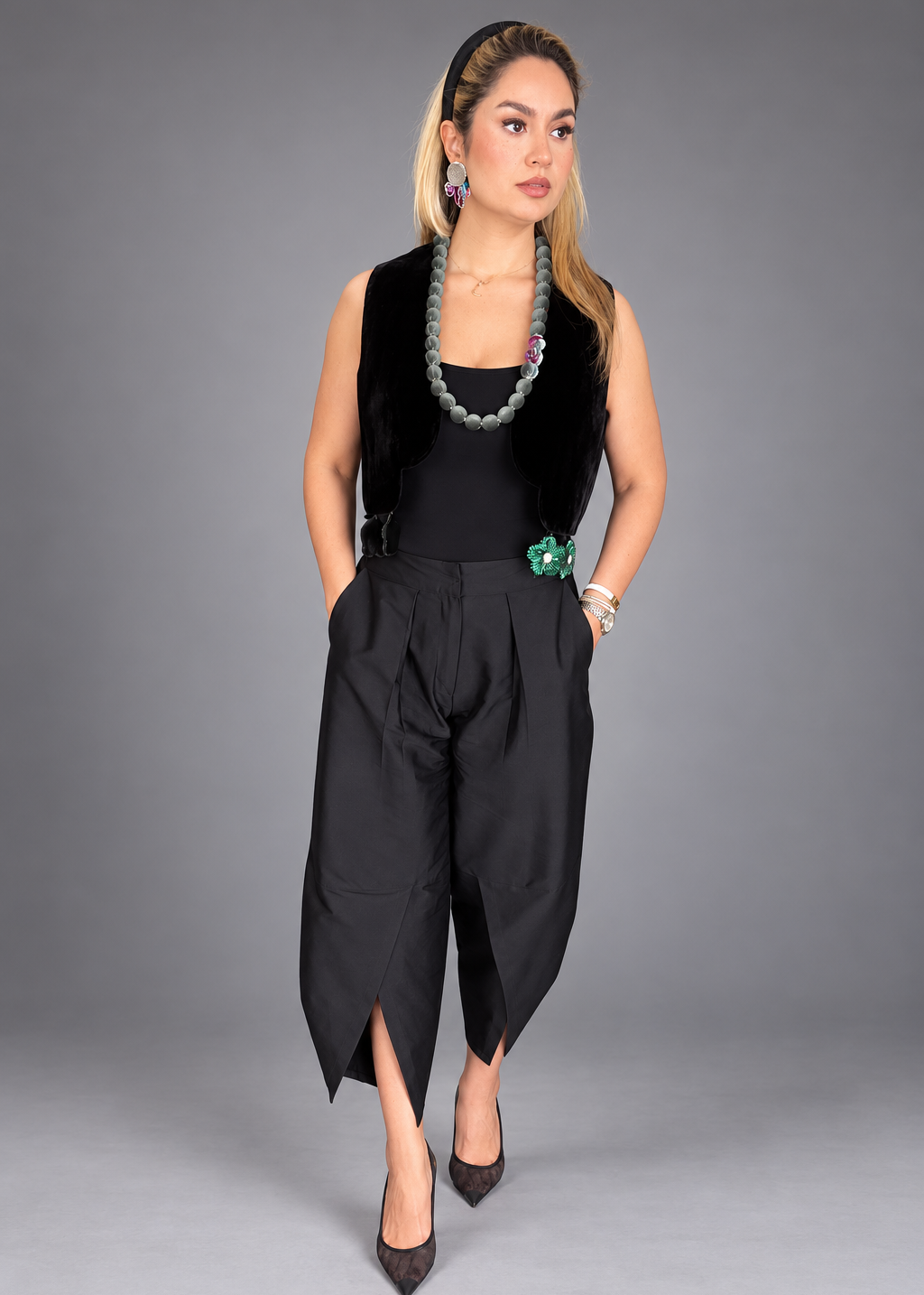 Woman wearing a colorful top and dark pants on a plain background