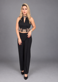 A woman modeling a black two-piece outfit consisting of a sleeveless crop top with gold floral embroidery and a matching high-waisted wide-leg pants, set against a solid gray studio background.