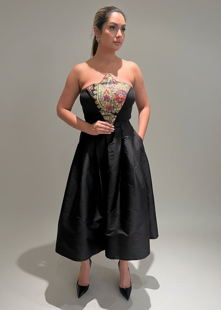 Woman wearing a black strapless dress with floral top on a plain background