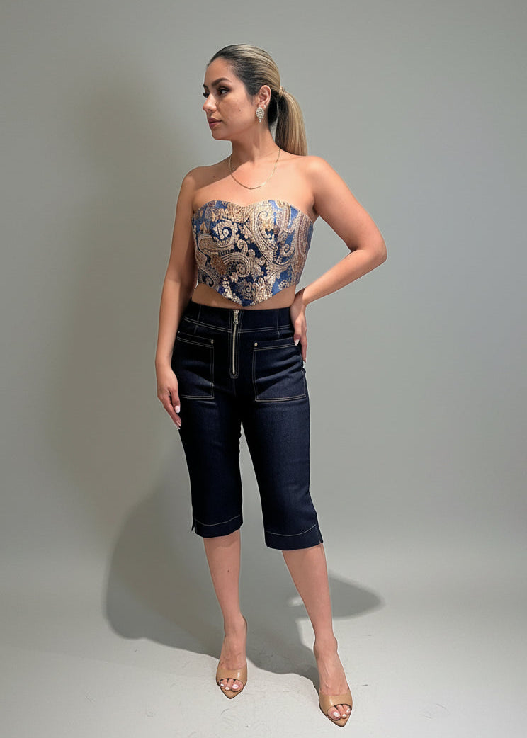 Woman wearing a strapless top and dark blue shorts against a plain background