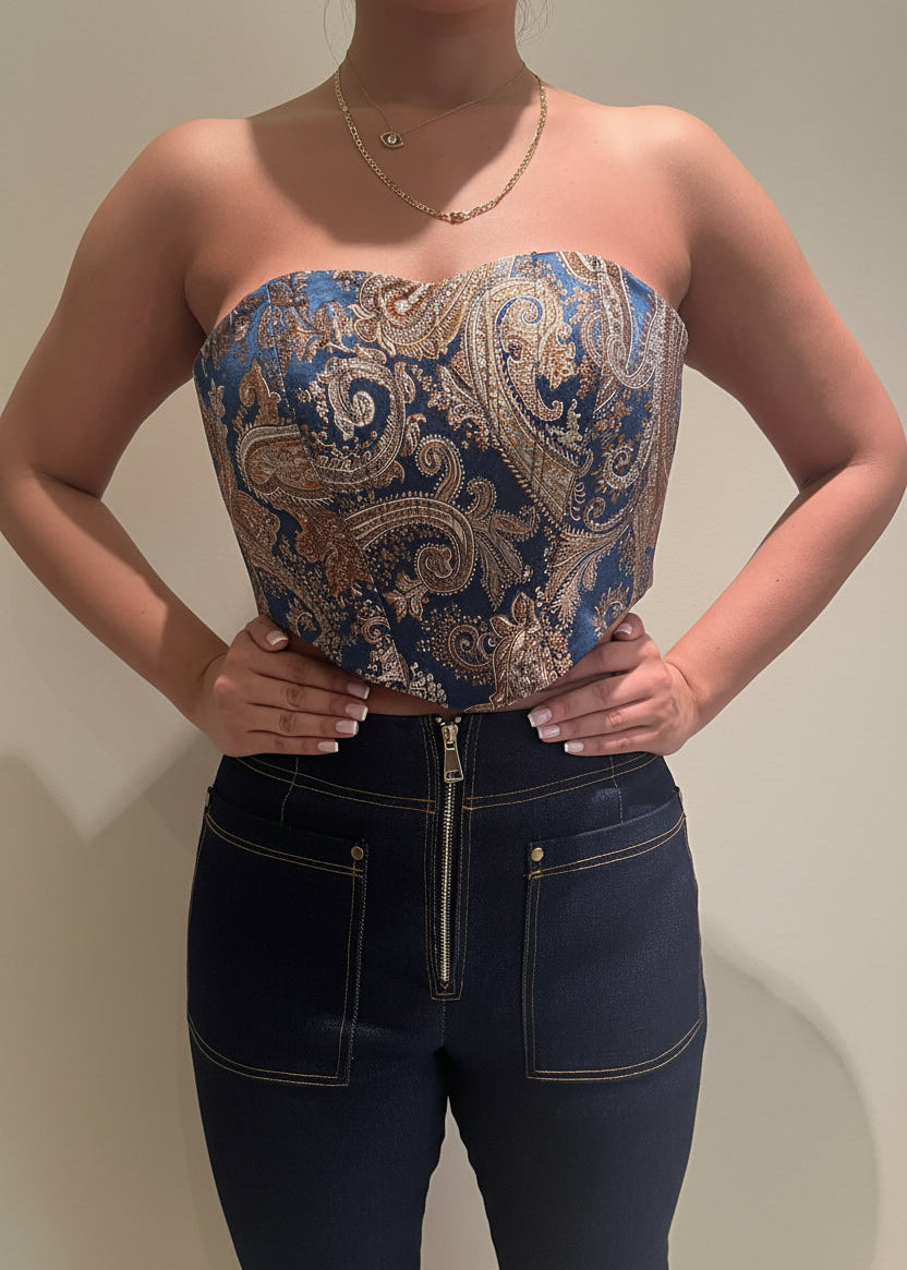 Person wearing a blue and gold paisley strapless top with dark jeans against a plain background